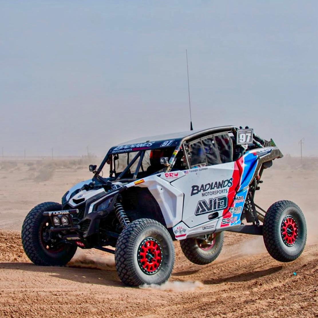 AVID Racing Can-Am Maverick X3 performance suspension kit mounted on vehicle racing on a dirt track